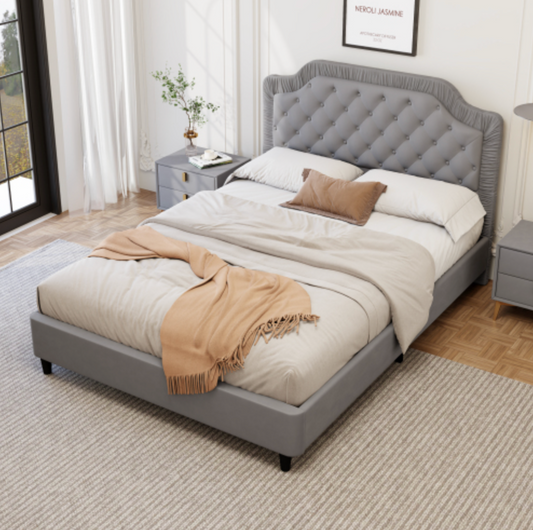 Gray upholstered bed with beige blanket and pillows in a bedroom setting.