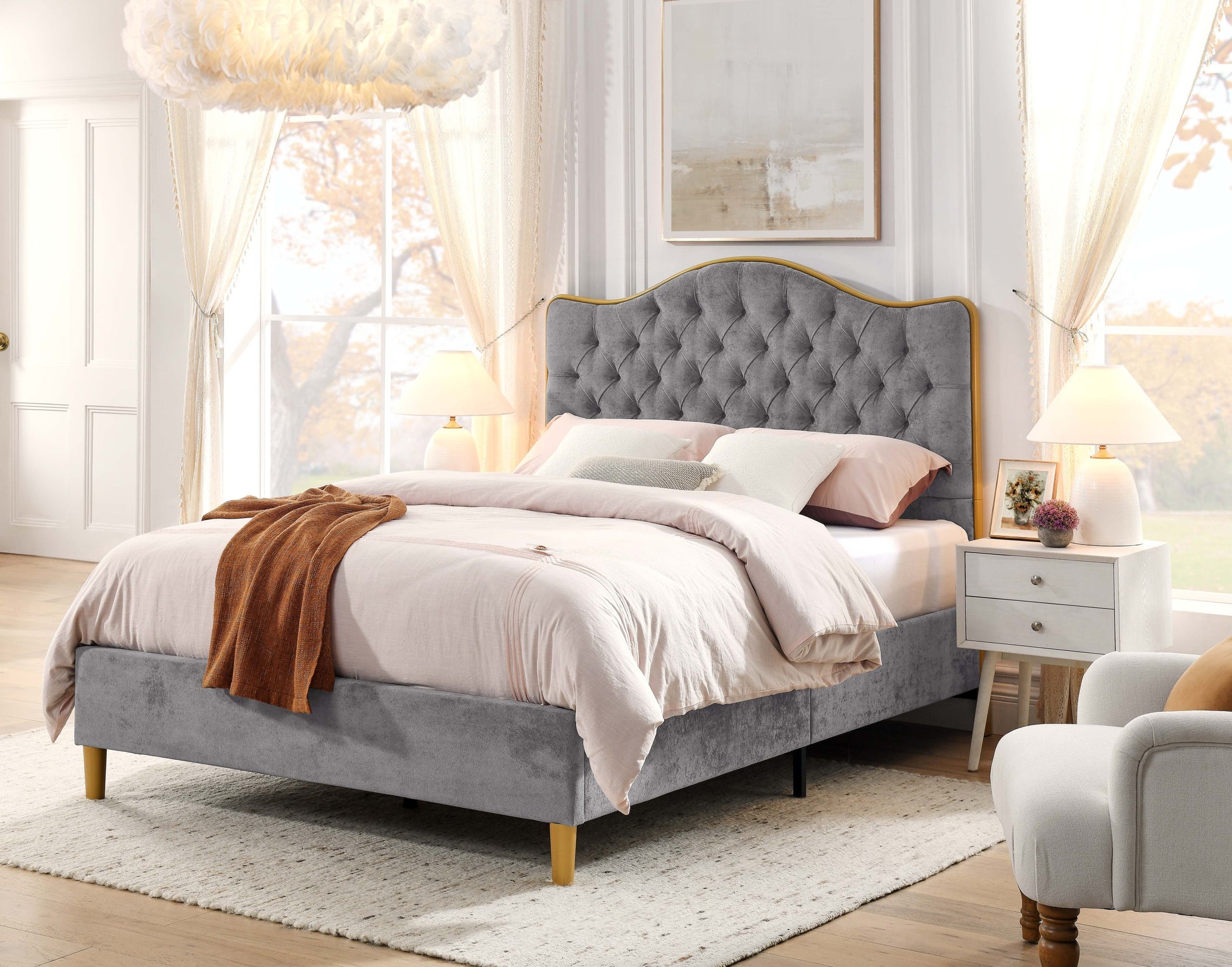 Gray upholstered bed in a bright bedroom with white walls and large windows.