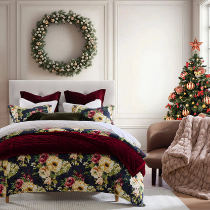Decorative floral bedspread on a bed with a Christmas tree and wreath in the background.