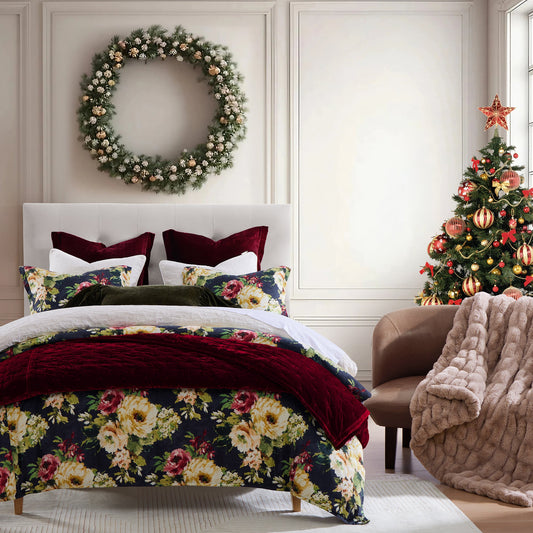 Decorative floral bedspread on a bed with a Christmas tree and wreath in the background.