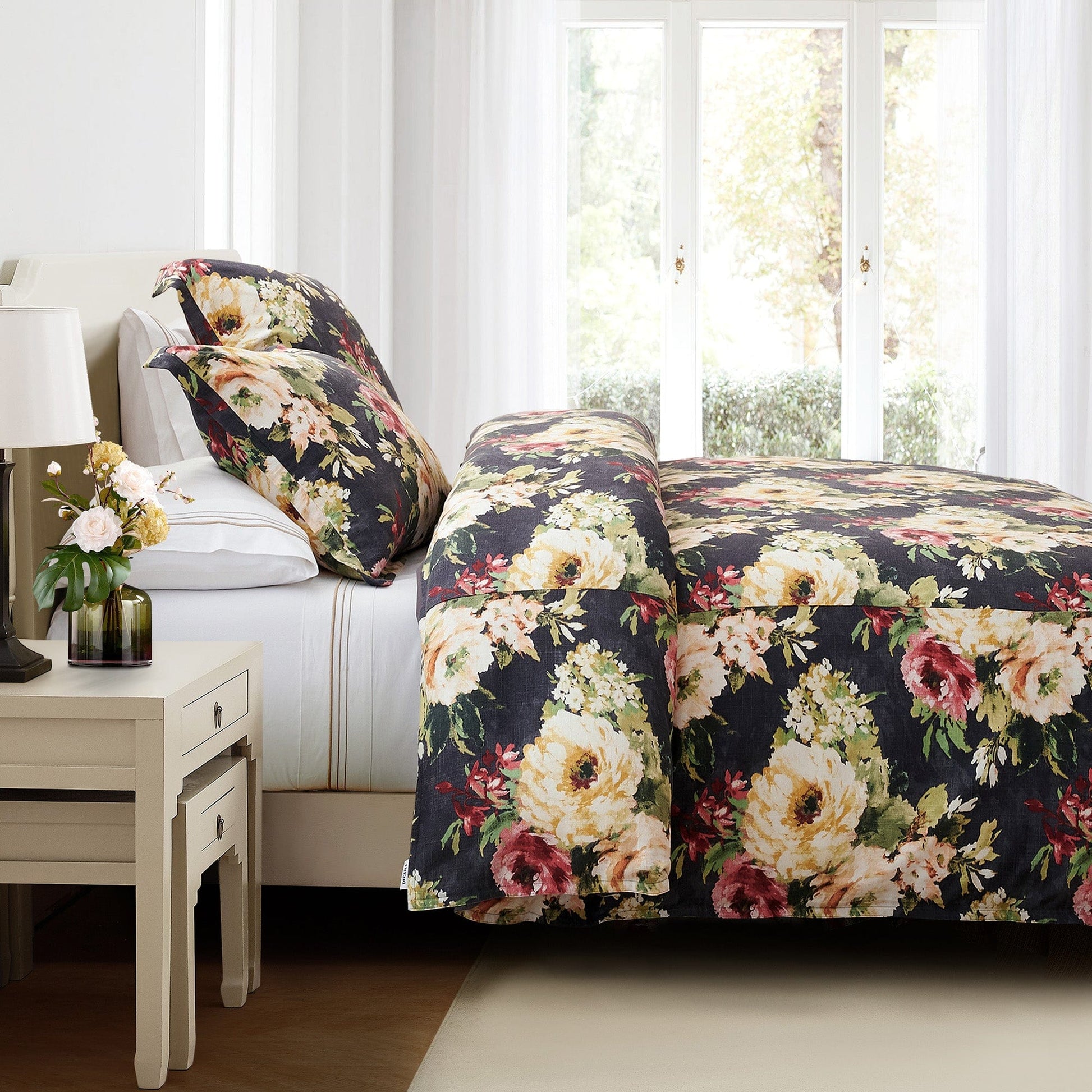 Floral bedding set on a bed in a bright bedroom with a side table and lamp.
