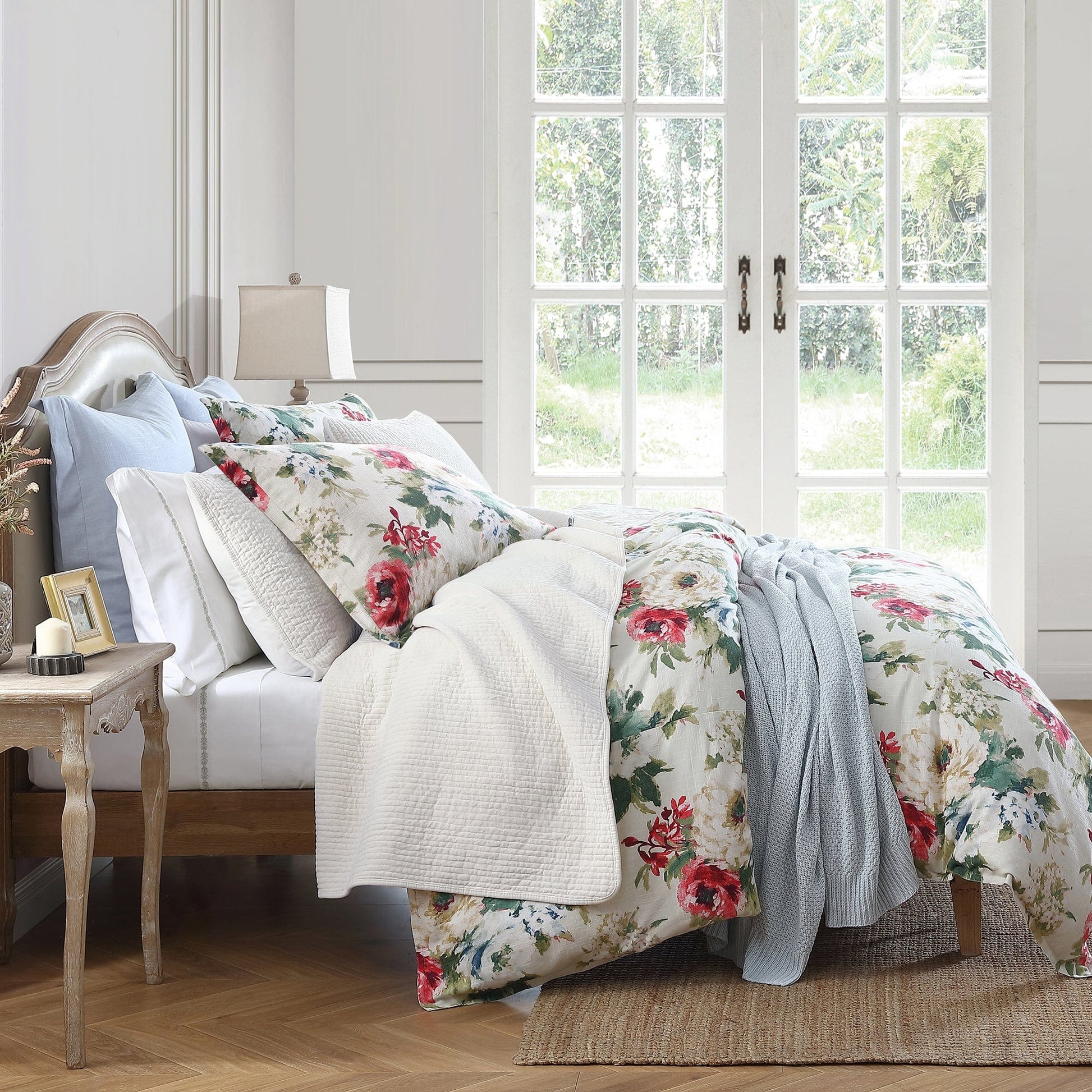 Floral bedding set on a bed in a bright bedroom with large windows.