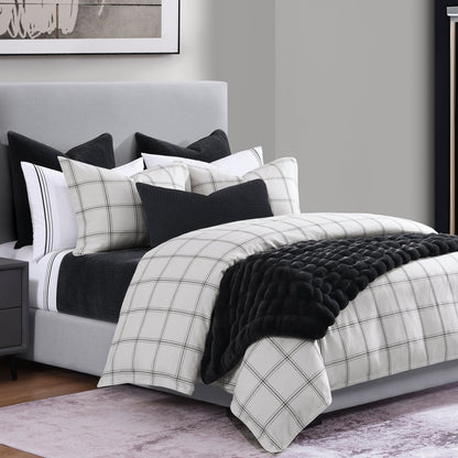 Bed with plaid comforter and black throw blanket in a bedroom setting