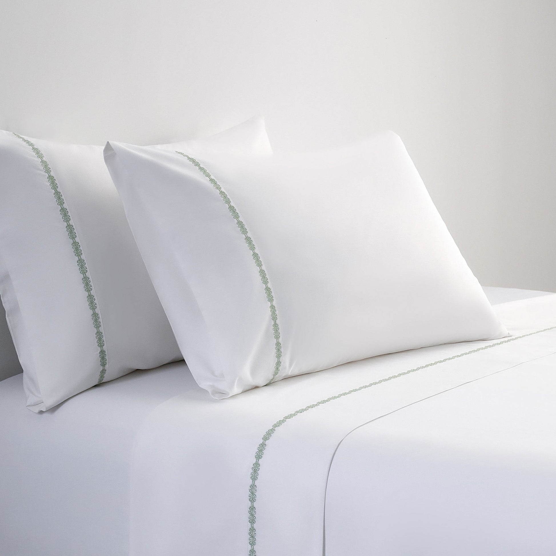 White pillows with green trim on a white bedspread