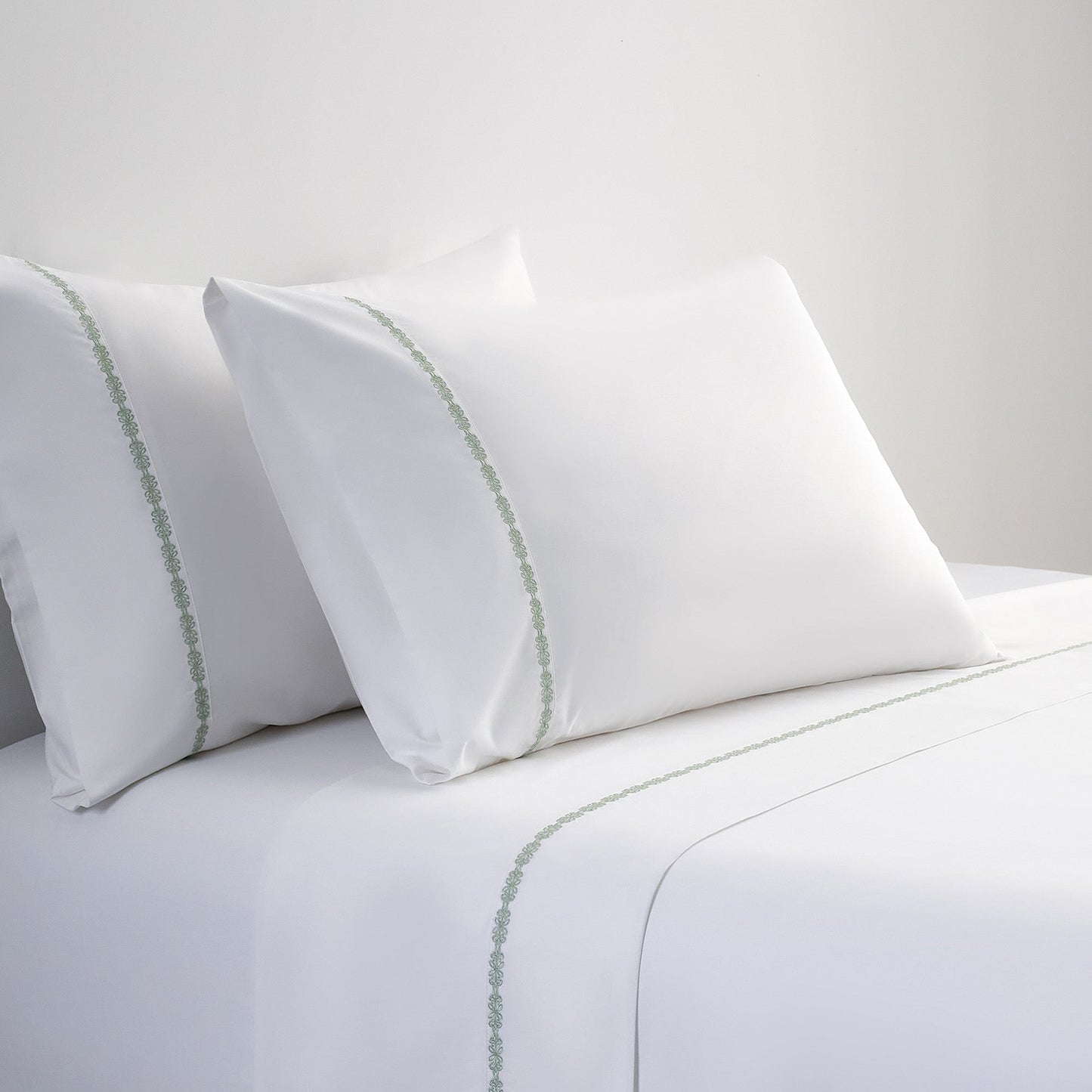 White pillows with green trim on a white bedspread