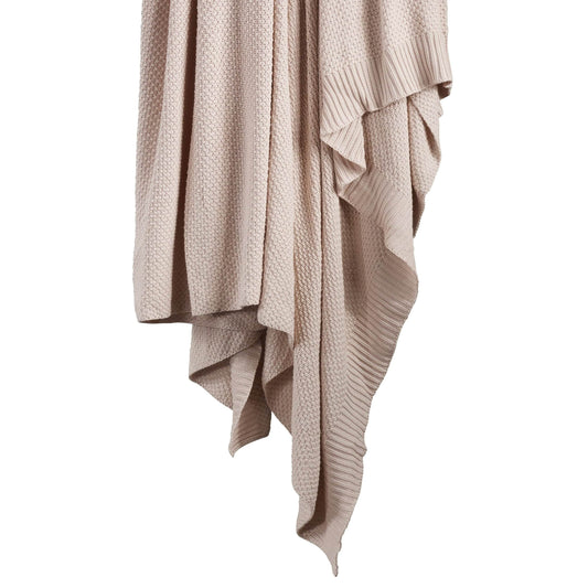 Beige knitted blanket draped over a white background