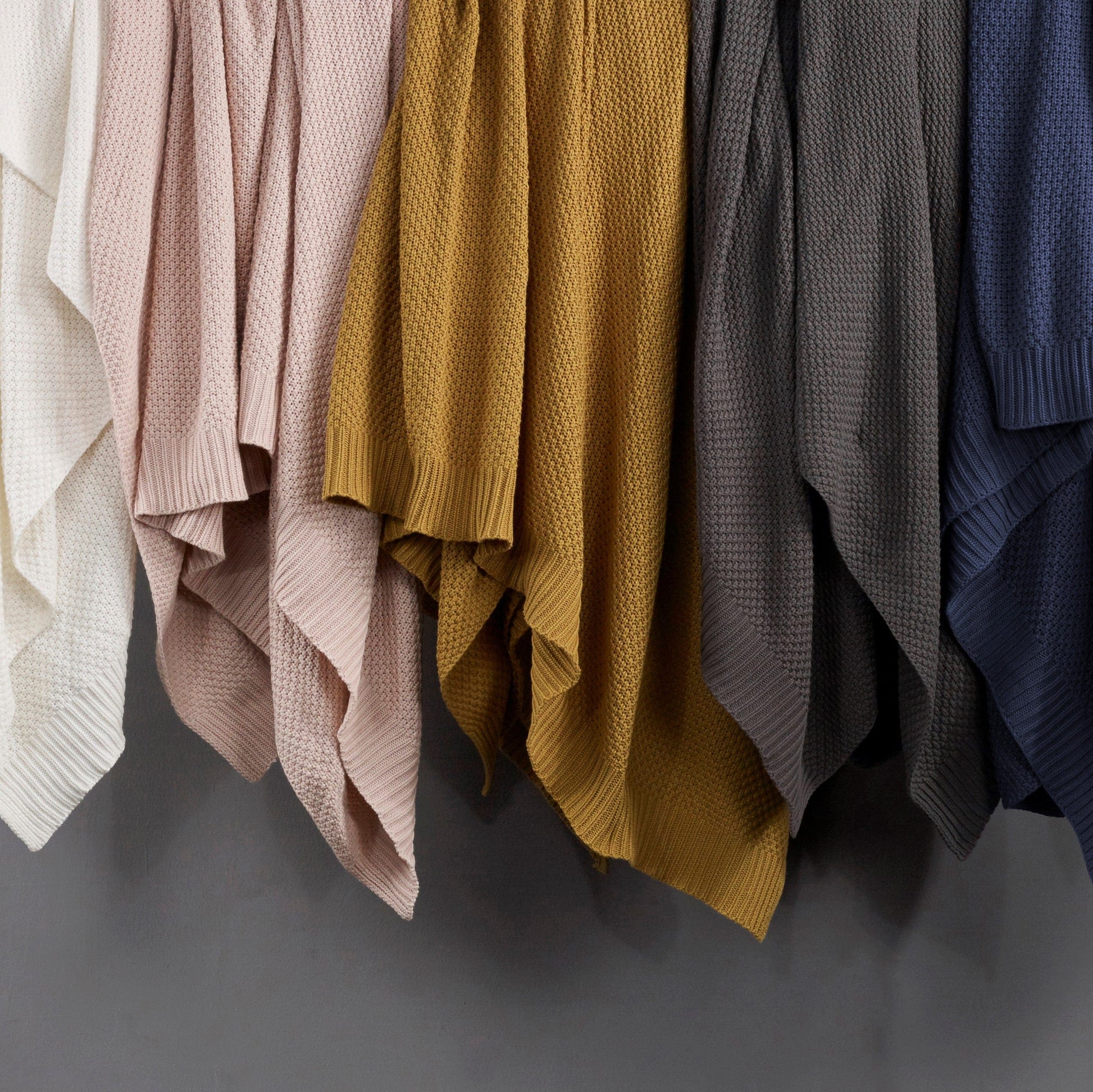 Collection of knit sweaters in various colors hanging against a gray background