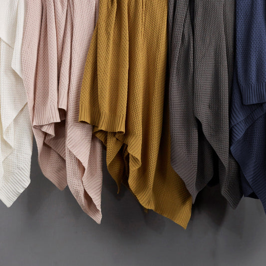Collection of knit sweaters in various colors hanging against a gray background