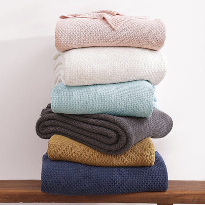 Stack of colorful knit blankets on a wooden surface with a light background