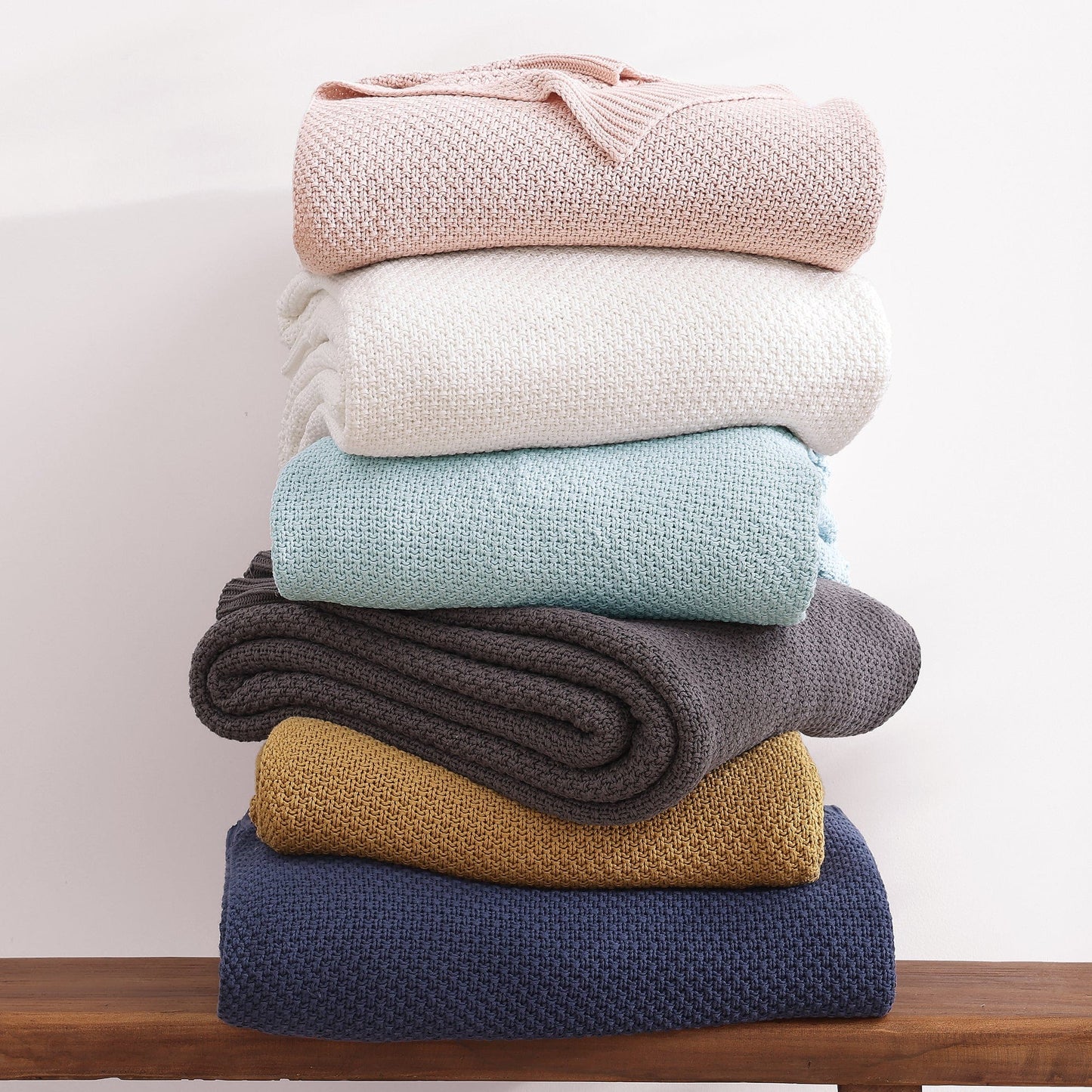 Stack of colorful knit blankets on a wooden surface with a neutral background