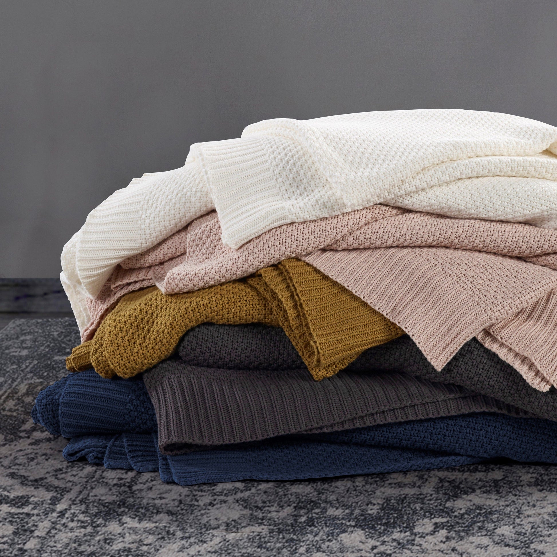 Stack of folded sweaters in various colors on a textured surface with a neutral background